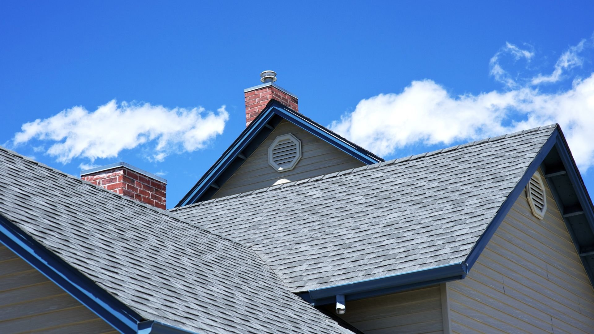 Gray shingled roof with brick chimneys against a bright blue sky